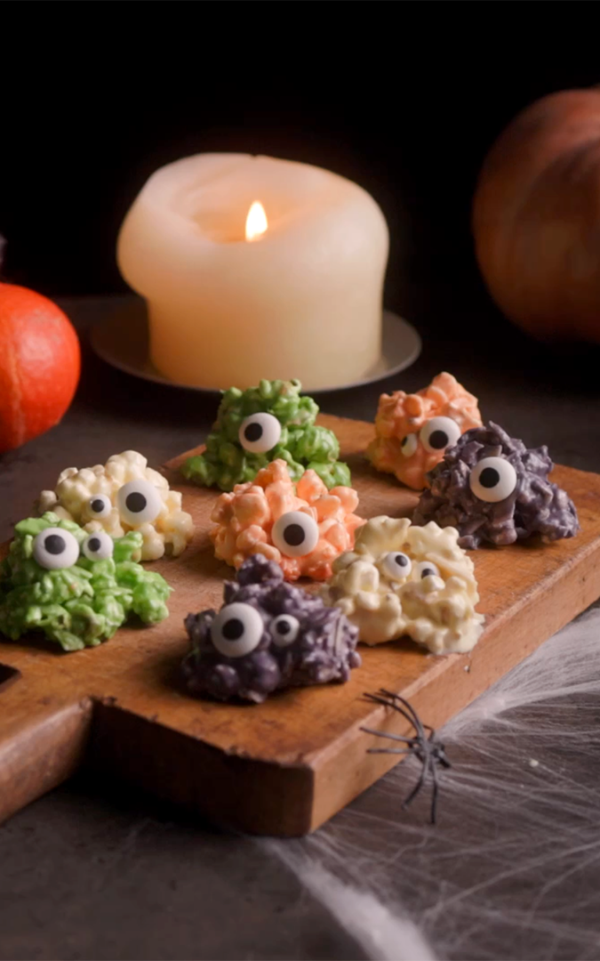 palomitas con chocolate de colores en forma de monstruos con ojos comestibles y decoración de halloween