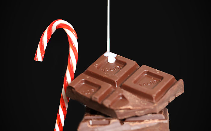 hilo de leche cayendo sobre una tableta de chocolate y un bastoncillo de caramelo de Navidad