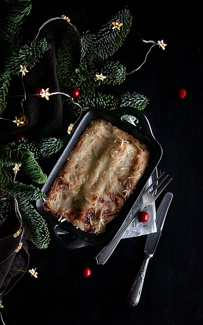 bandeja de horno con canelones gratinados con adornos de navidad al fondo