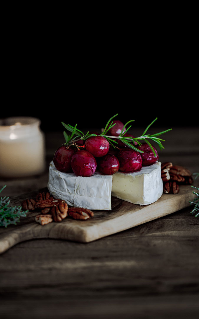 Round camembert cheese open, with red grapes on top and Christmas ornaments