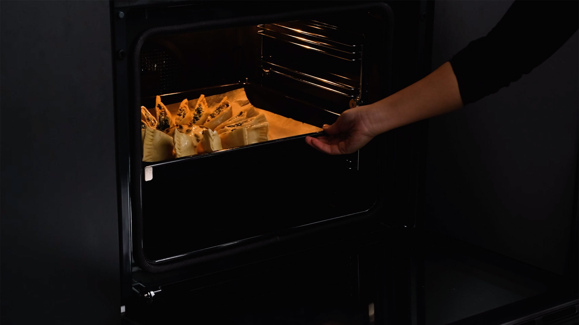 hand placing a tray with spinach and cheese recipe inside a Teka oven 