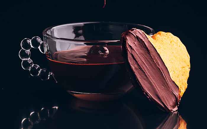 Galleta con forma de corazón apoyada en taza de cristal con chocolate dentro
