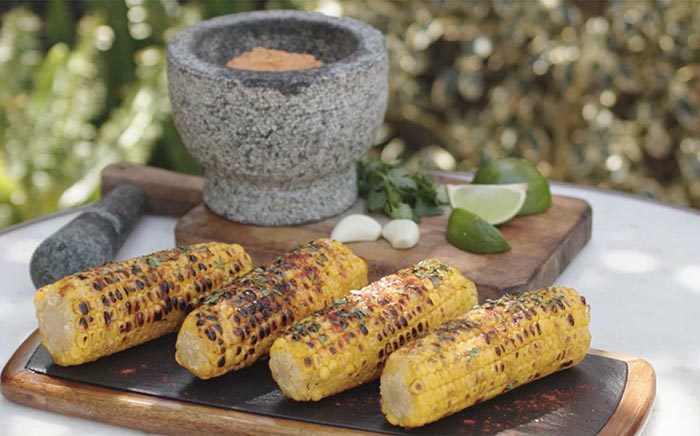 Mazorcas de maíz a la parrilla con tabla de madera detrás con mortero barbacoa vegana