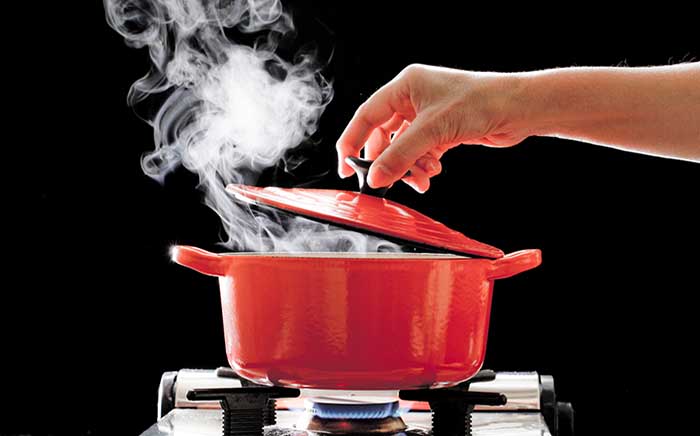 Red pan over low heat cooking food while a hand put the lid on