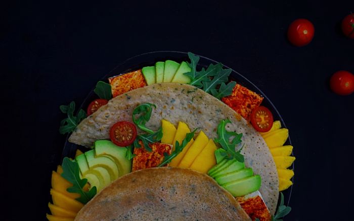 Crepes salados con aguacate, tomate y otras verduras multicolor sobre fondo negro