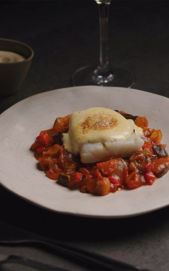 Plate with bake cod and aioli with a bed of vegetables and a glass of white wine on one side