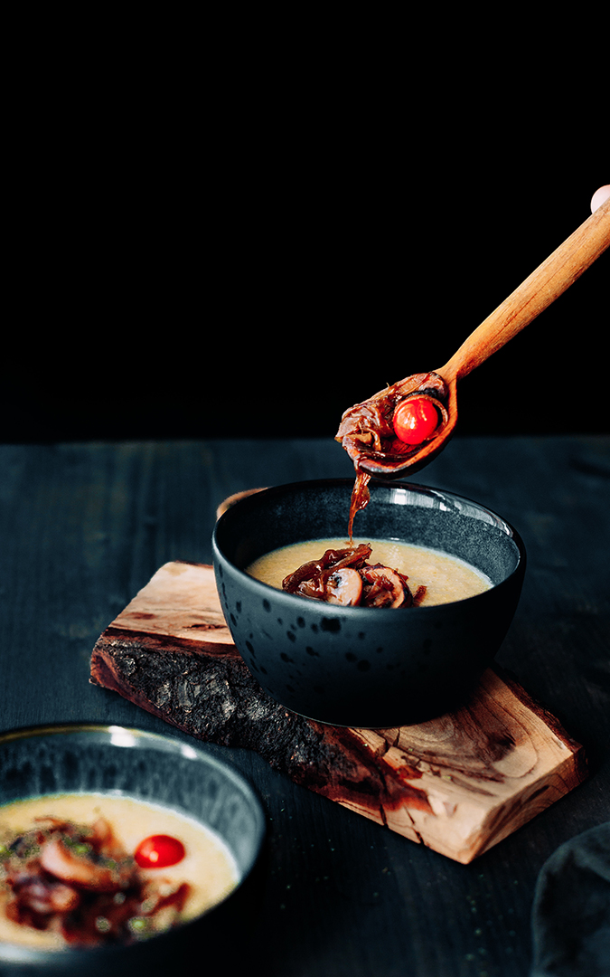 Two bowls with roasted veggies and mushrooms and creamy polenta with a wooden spoon