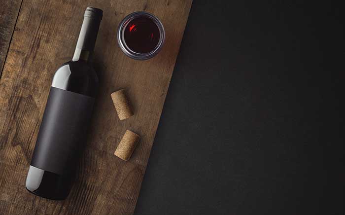 Botella de vino tinto sobre tabla de madera con corchos y una copa de vino