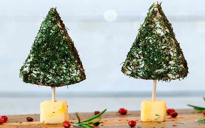 Arbolitos de Navidad hechos de queso con eneldo sobre un cubo de queso
