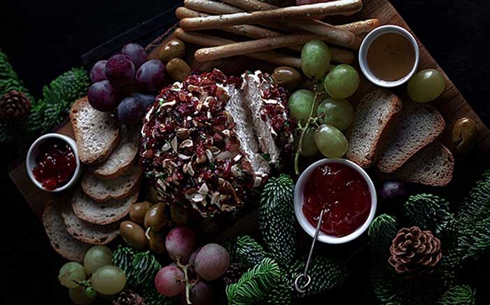 Bandeja con aperitivos queso de Navidad vegano, uvas, tostadas, salsas y adornos navideños