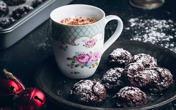 Taza de porcelana con cacao y unas galletas de chocolate con azúcar glass rodeadas de decoración de Navidad